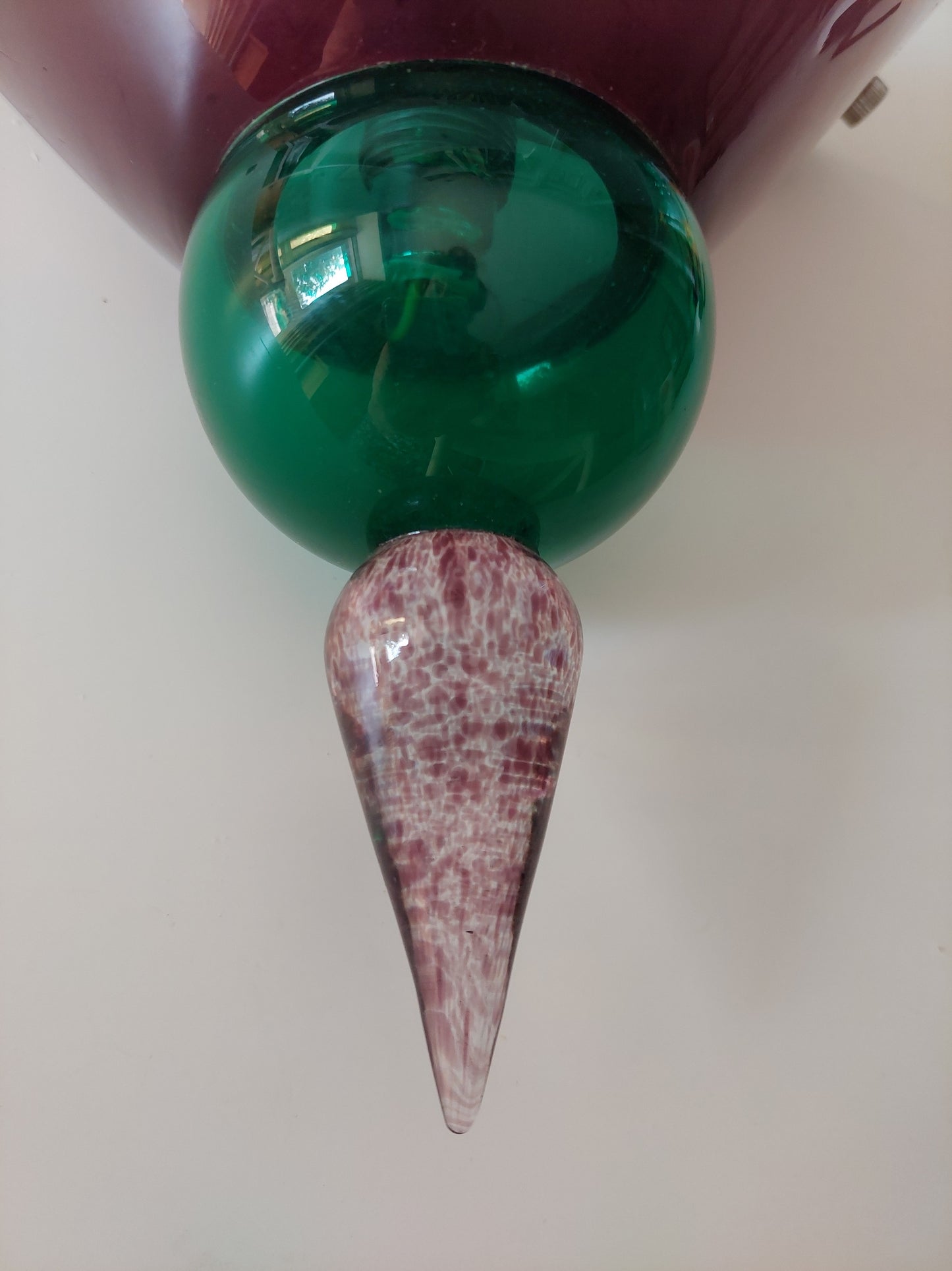 A close-up of a glass wall sconce featuring a glossy green spherical shade, a conical drop with a marbled pink and white pattern, and a dark burgundy glass upper section.