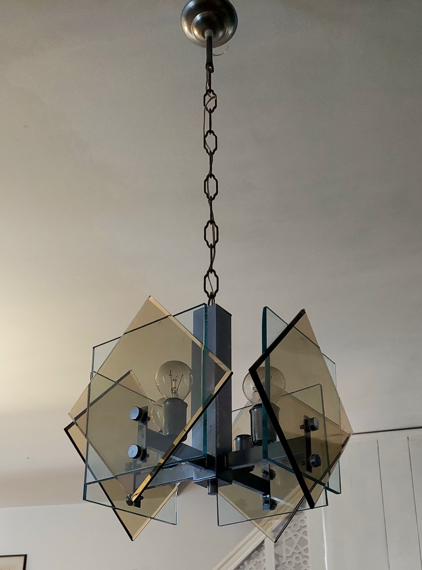 A modern geometric chandelier with translucent amber-tinted glass panels and a dark metal frame, hanging from a ceiling in an indoor room.
