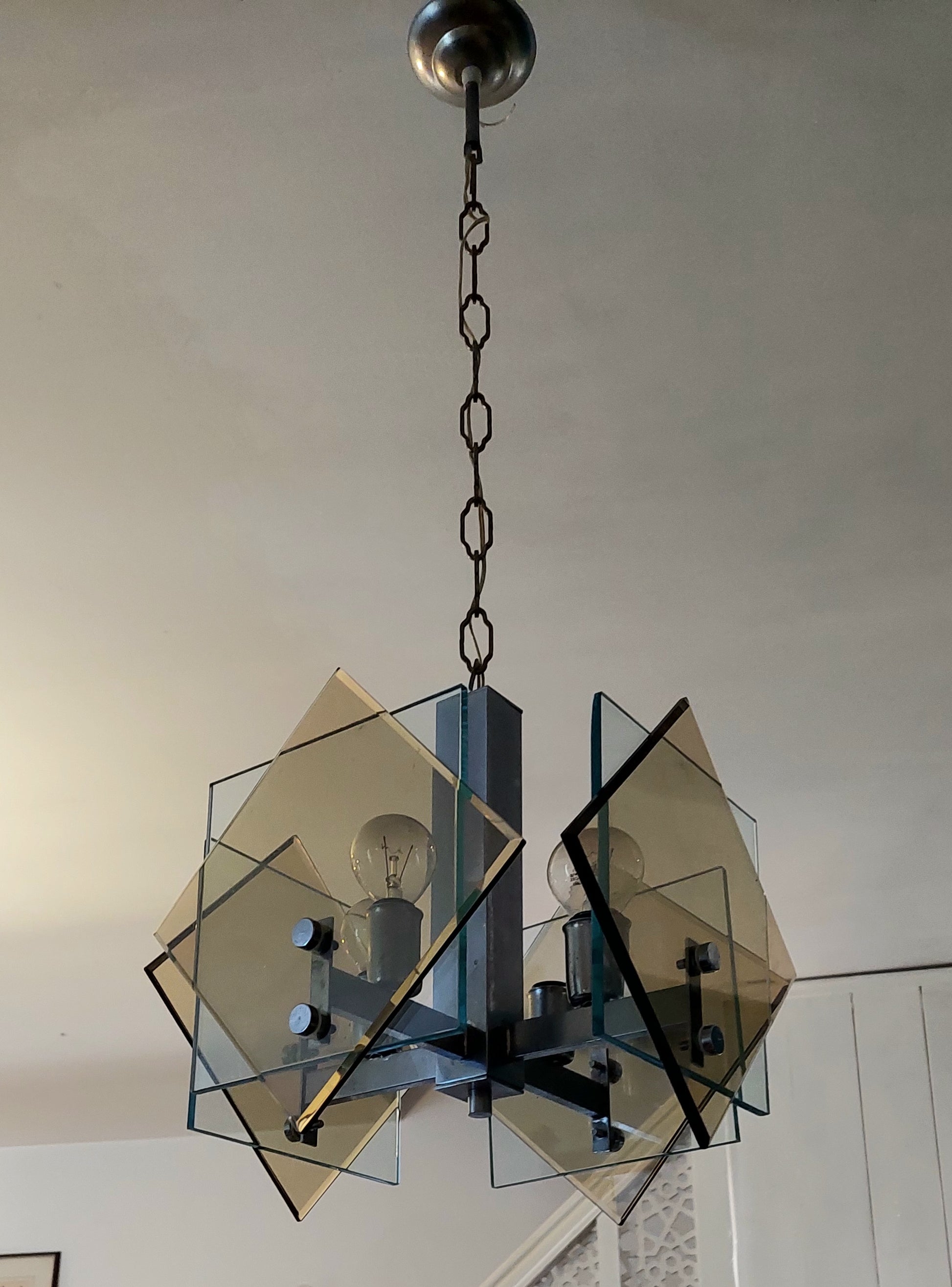 A modern geometric chandelier with translucent amber-tinted glass panels and a dark metal frame, hanging from a ceiling in an indoor room.