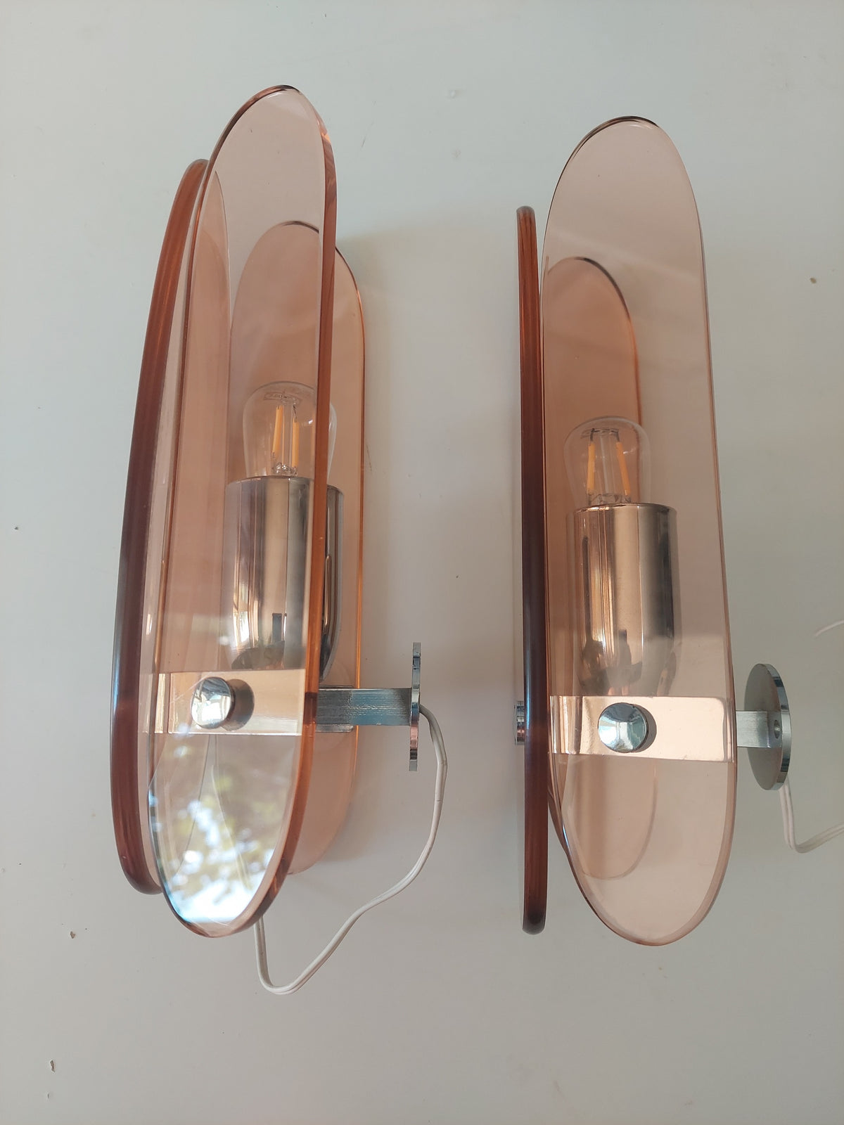 A pair of mid-century modern wall sconces with translucent rose-tinted glass shades and brushed copper metal accents, shown against a plain off-white wall.