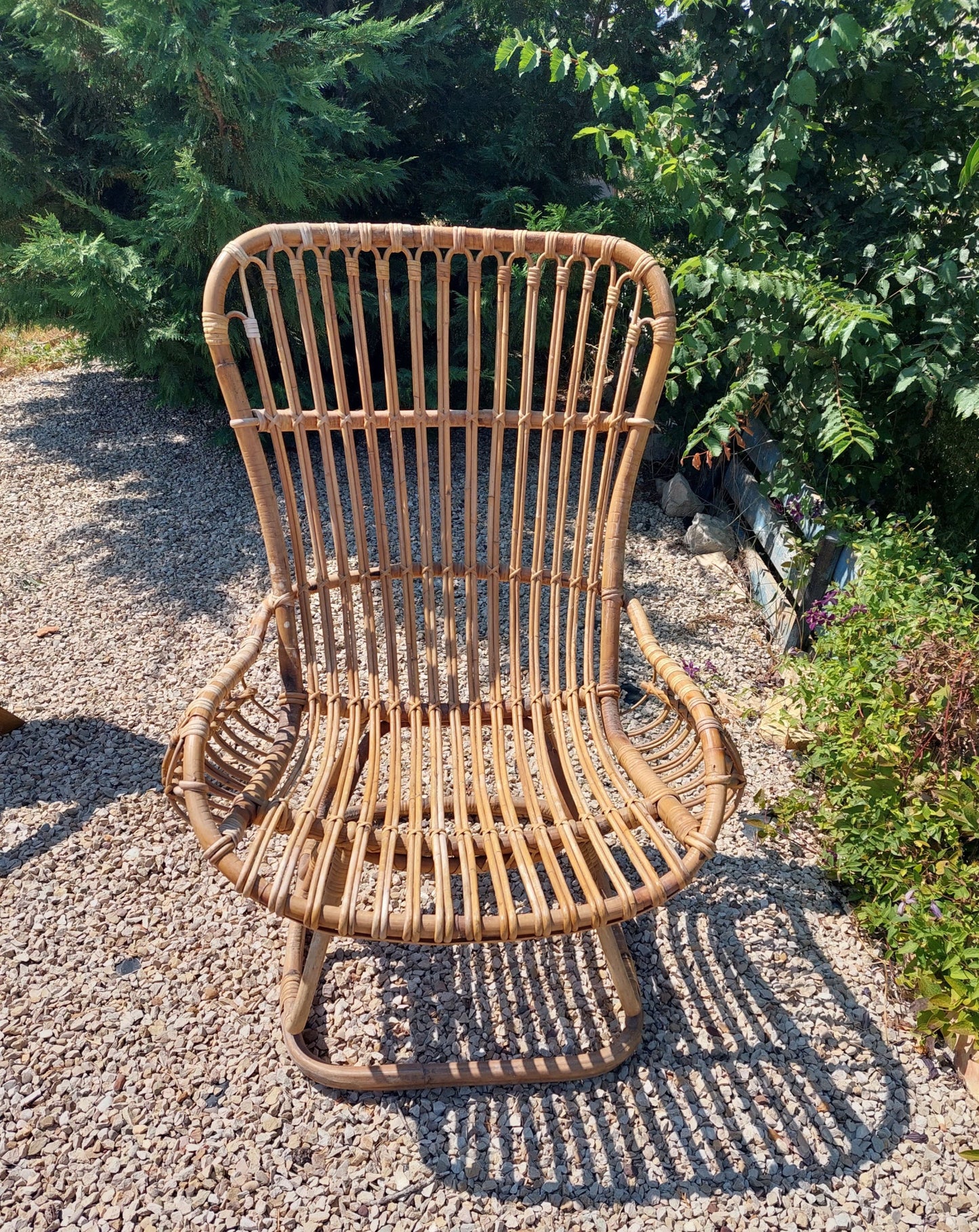 Wicker chair on a gravel surface with greenery in the background